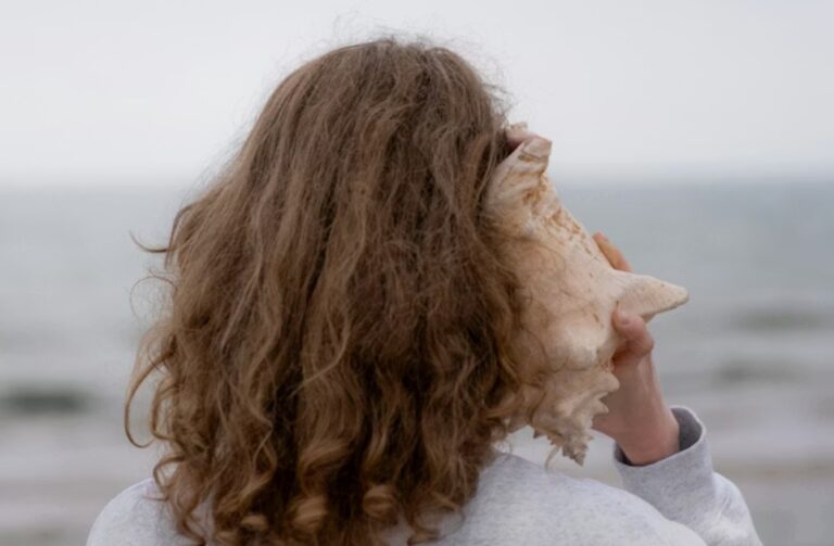 woman at the beach with a conch shell up to her ear